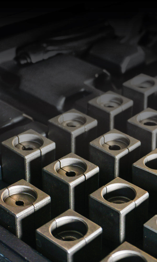 Close-up of metallic square components with circular openings arranged in a grid pattern. The image conveys precision and industrial craftsmanship.
