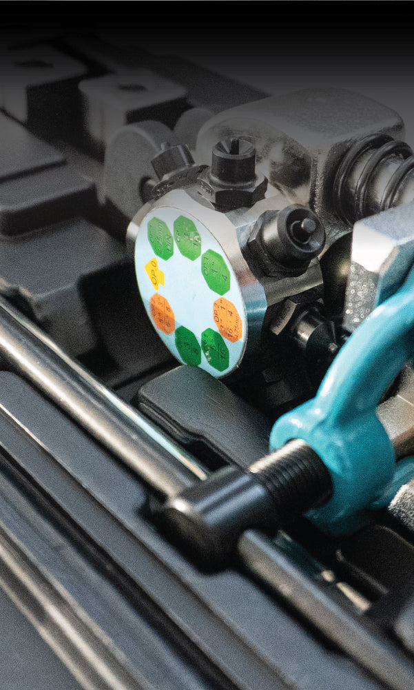 Close-up of a mechanical device with a circular dial featuring colored markers, alongside various metal components and a blue clamp.
